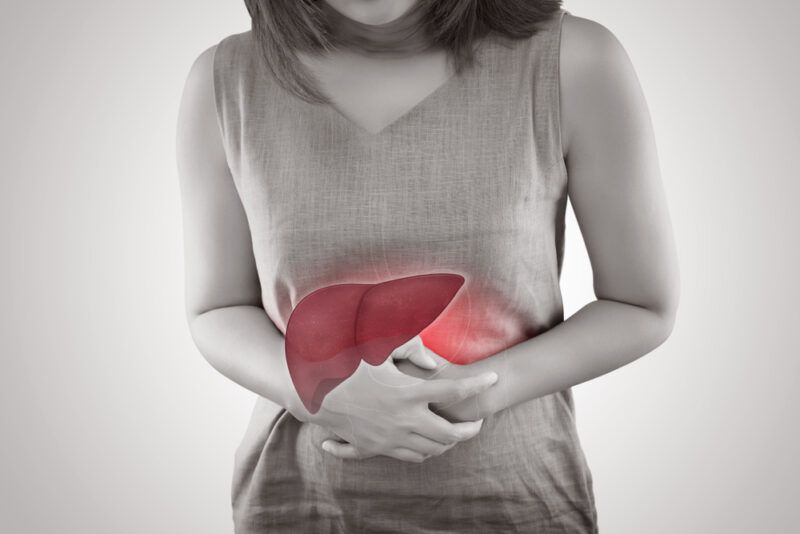 The,Photo,Of,Liver,On,Woman's,Body,Against,Gray,Background, | Food For Net This photo shows a black and white image of a woman holding her abdomen, behind an overlay of a red, inflamed liver, representing the best foods for liver disease.