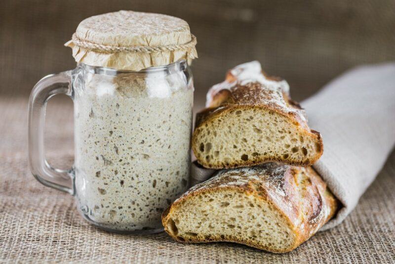 Two loaves of sourdough bread, next to a mug of the starter culture