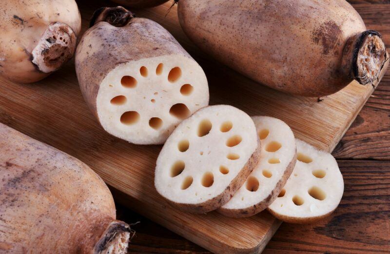 Lotus roots on a table, including one that has been sliced to reveal pieces with a ring of holes