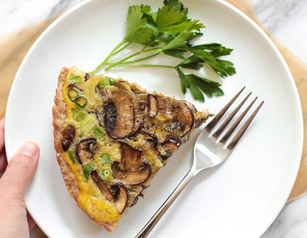 A slice of mushroom quiche on a plate with a fork.