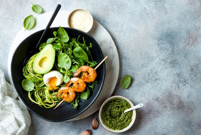 A black keto bowl with shrimp, avocado, pesto and zoodles