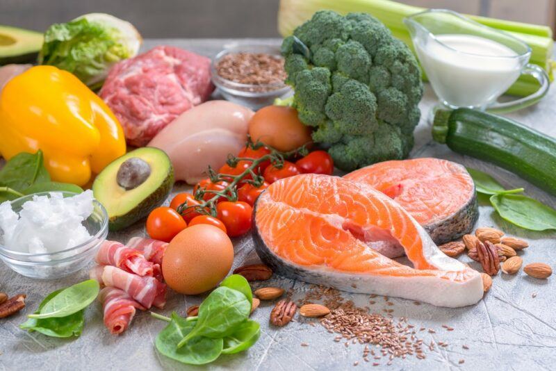 A collection of low carb or keto foods on a table, including salmon, avocados, chicken, and more