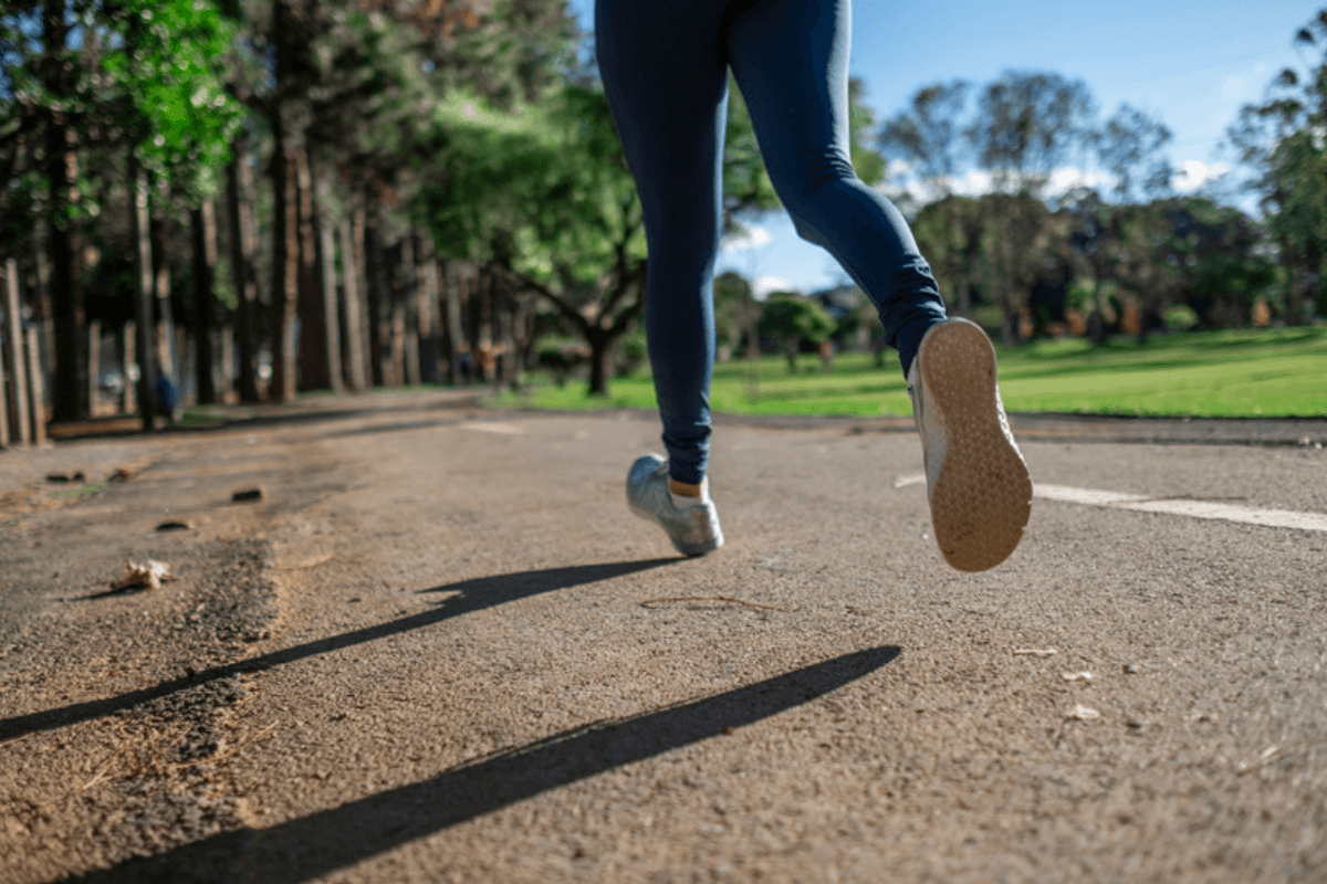 Lower half of a runner running on the road on a sunny day with green trees surrounding the trail