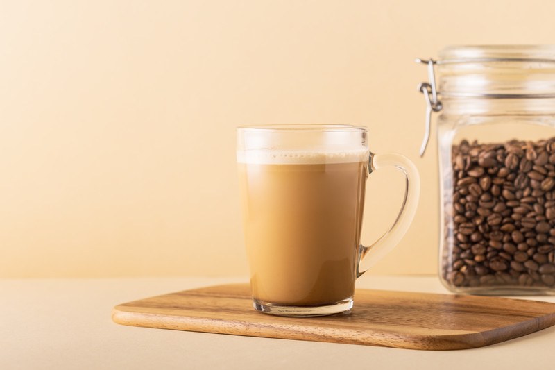 A cup of coffee blended with MCT Oil and butter rests on a cutting board near a glass canister of coffee beans.