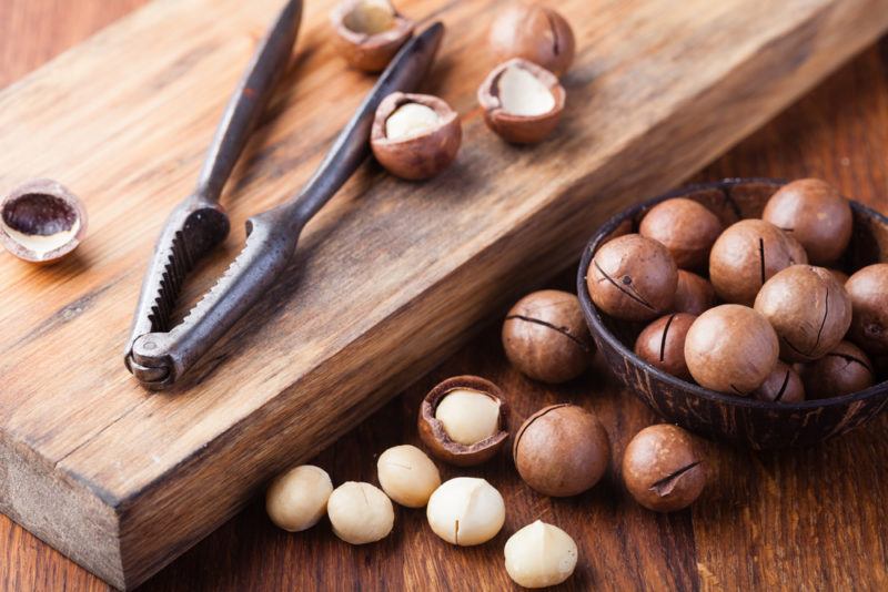 Macadamia nuts being cracked on a board and next to it