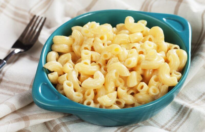 A blue container containing mac and cheese, next to a fork