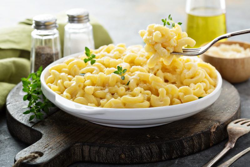 A white dish of macaroni cheese next to salt and pepper, with some being taken out on a fork