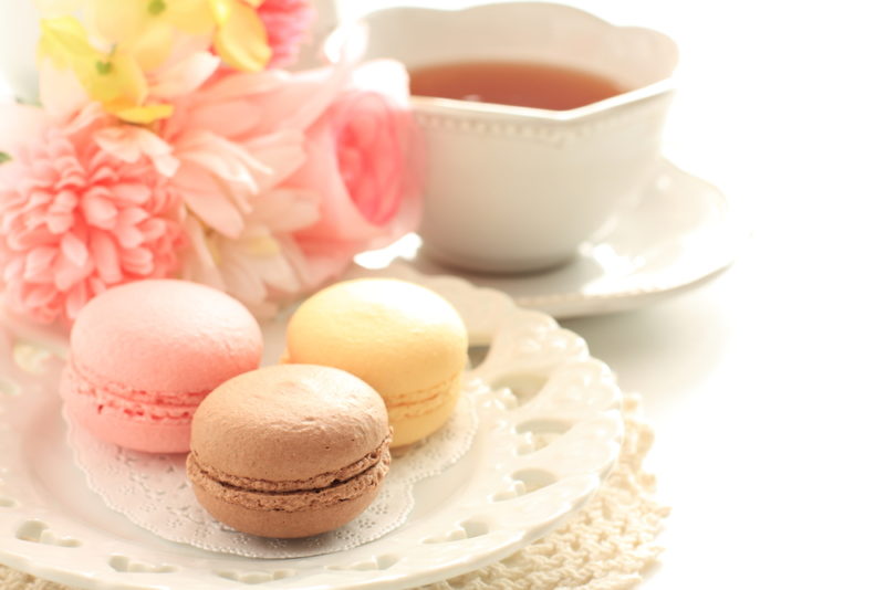 A white plate with three macarons with a mug of tea in the background