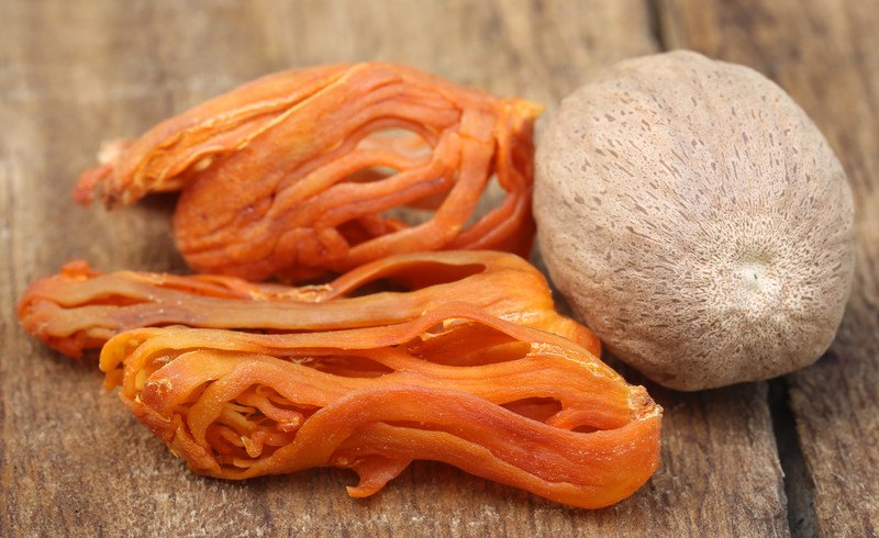 Closeup image of mace with a nutmeg seed resting on a wooden table.