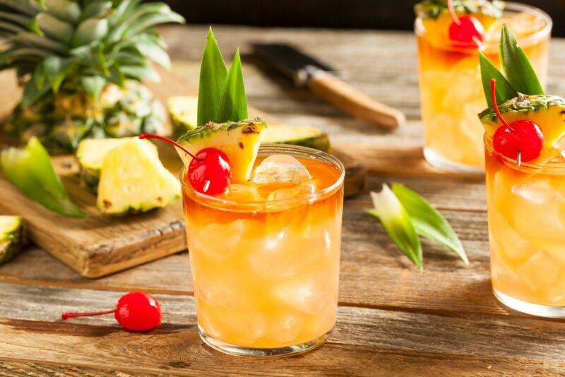 A wooden table with three mai tais with pineapples and glace cherries