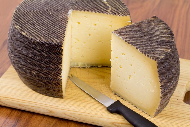 Manchego cheese wheel on a cutting board with a wedge cut out of it