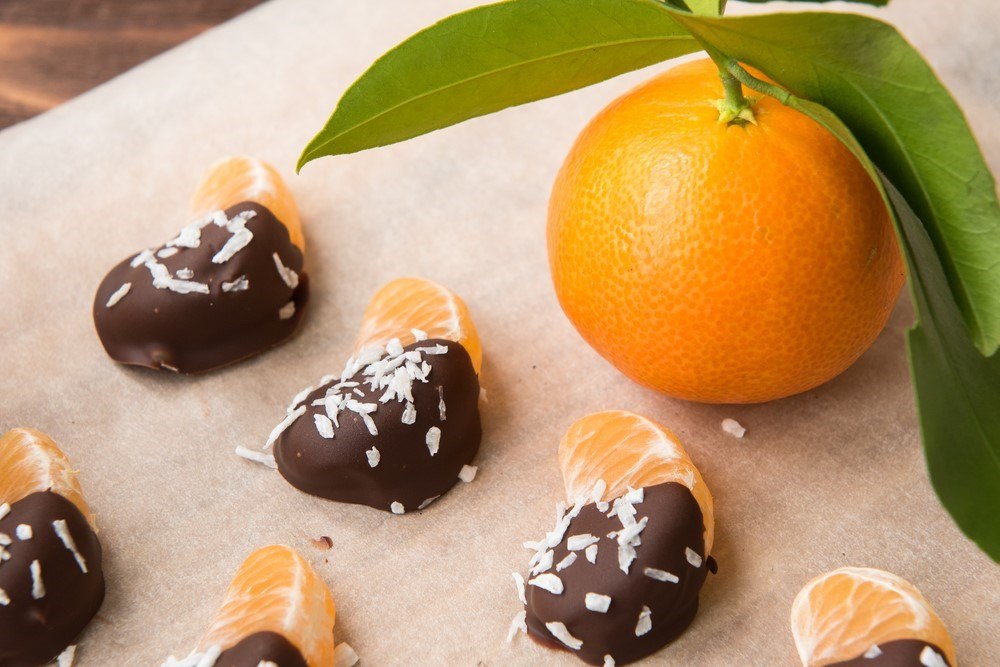 Mandarin slices on a wooden board that have been dipped in chocolate and sprinkled with coconut