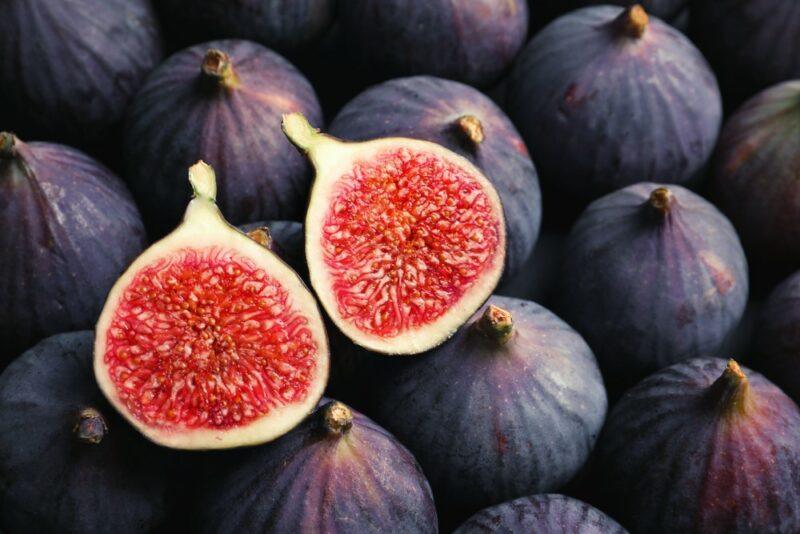 A pile of fresh purple figs, with one that's been sliced in half