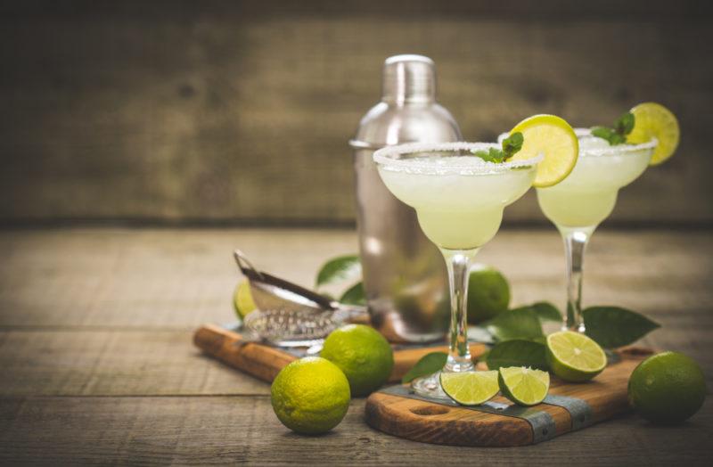 Two margaritas with a cocktail shaker and limes