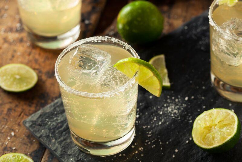 Three margaritas with ice and lime on a table with more limes surrounding them