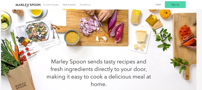 White table with fresh ingredients and people chopping veggies on a board. 