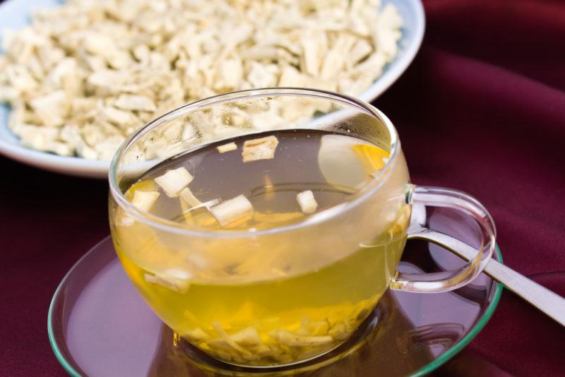 A glass mug of tea next to a bowl of marshmallow root