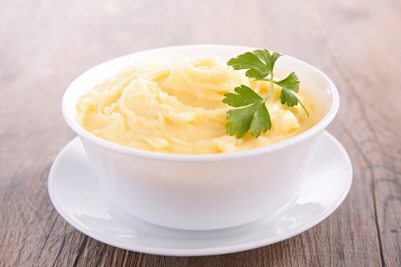 A white dish is filled with masked potatoes and a sprig of parsley.