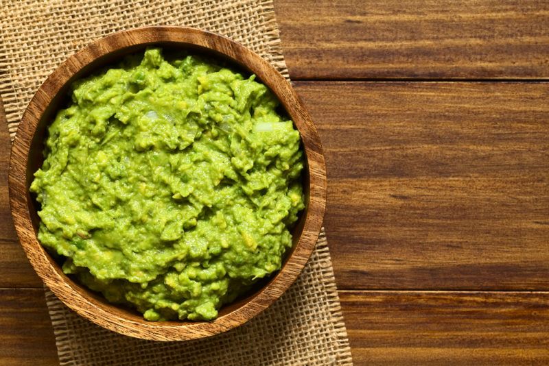 A wooden bowl containing mashed avocados on a table