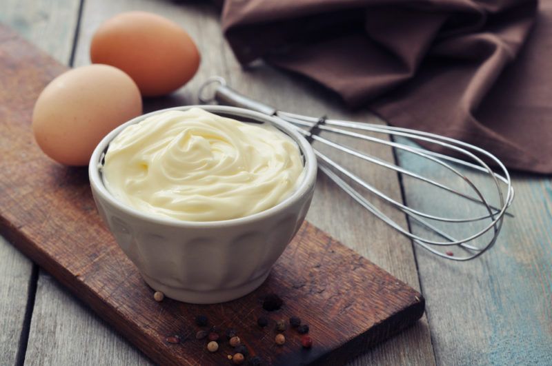 A bowl of mayonnaise with eggs and a whisk