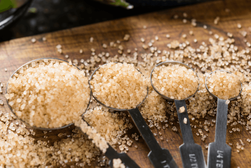 A wooden board with a collection of measuring spoons that contain different amounts of raw sugar.