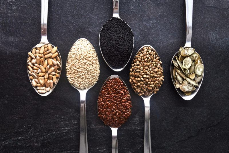 Metal spoons facing up and down that each contain a different type of seed