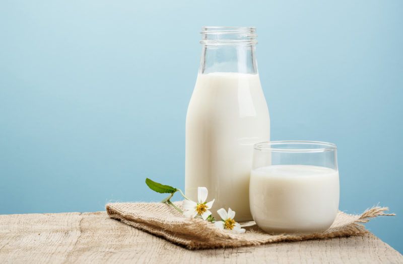 A bottle of milk and a glass of milk on a table against a blue background