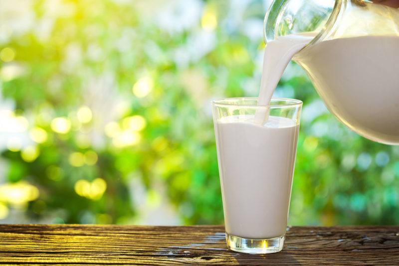 Milk being poured from a jug into a glass on a wooden table outdoors