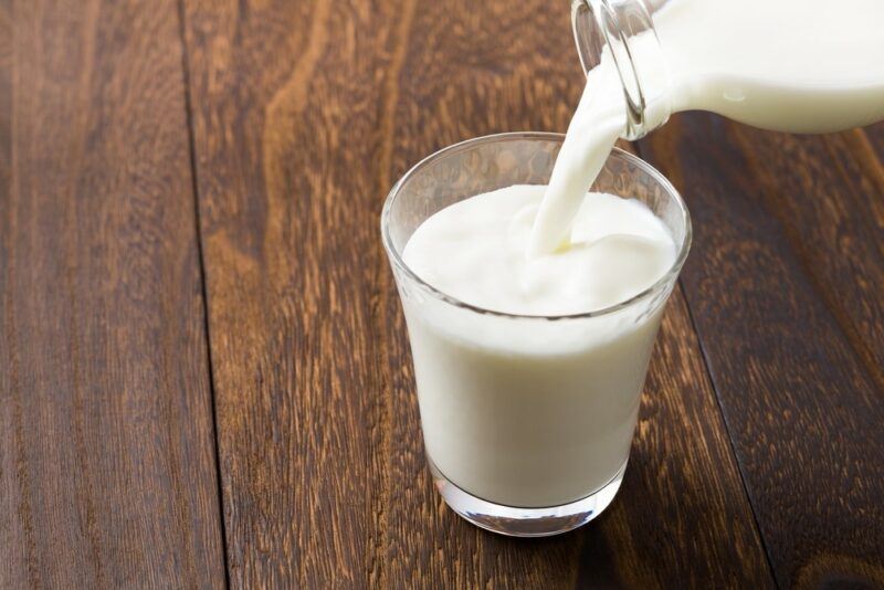 A wooden table with a glass of milk being poured from a bottle