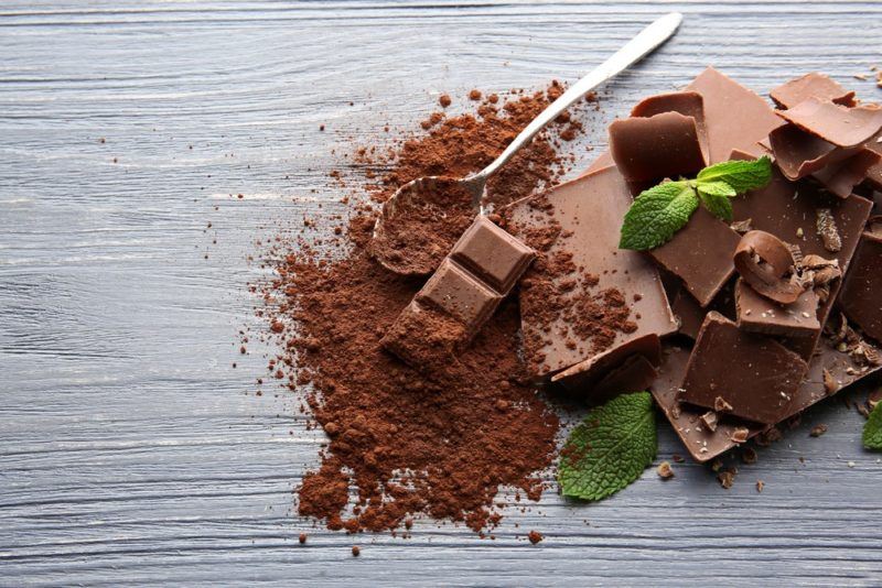 Milk chocolate on a gray table, including cocoa powder, a spoon, and some mint leaves