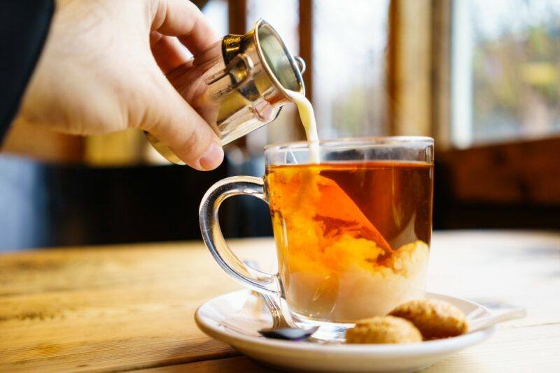 A glass of hot black tea with someone pouring cream or milk into it