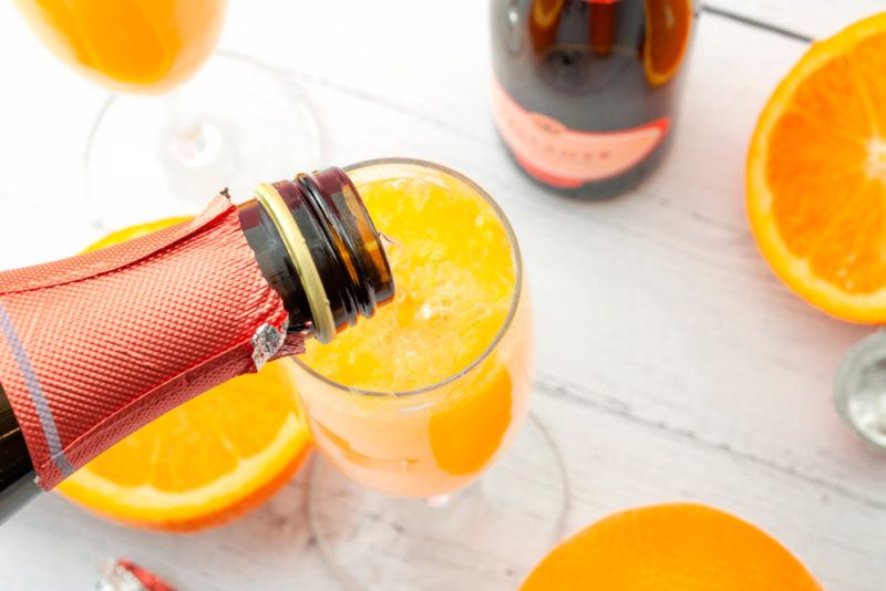 Pouring white sparkling wine into a glass of orange juice