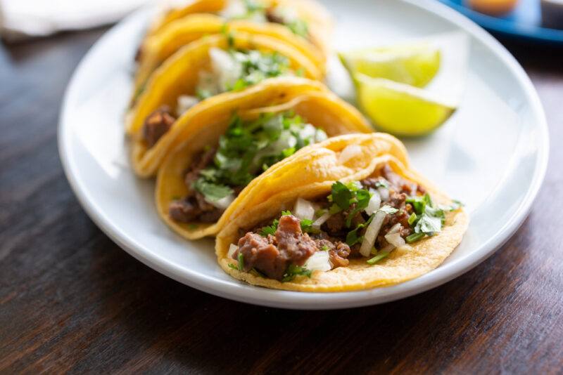 A white plate holds a row of mini tacos and some lime slices.