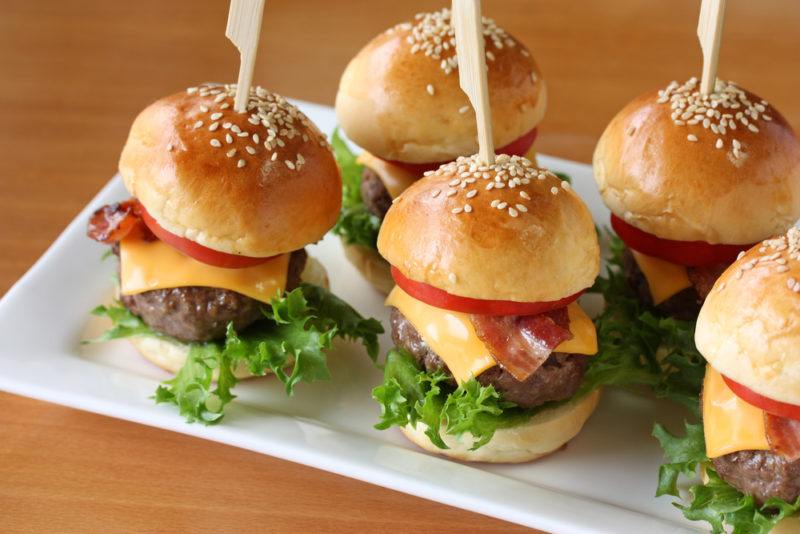 A white plate that contains give mini hamburgers for a party