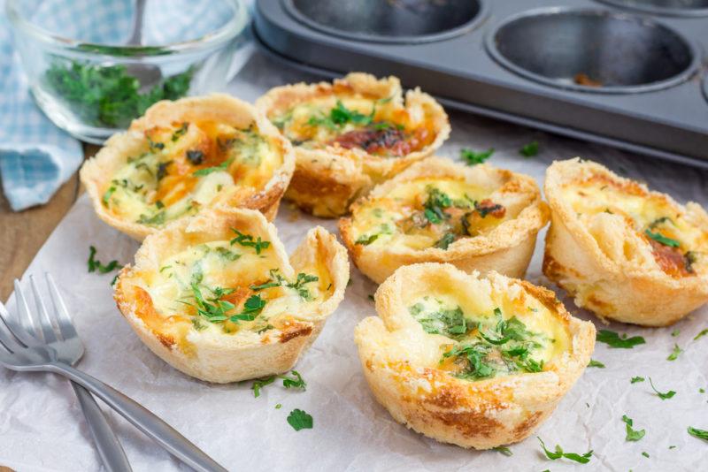 Fresh mini quiches on baking paper in front of a baking tray