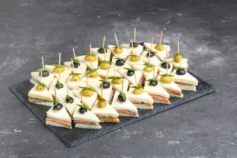 A black tray that contains mini sandwiches, each with a toothpick through it