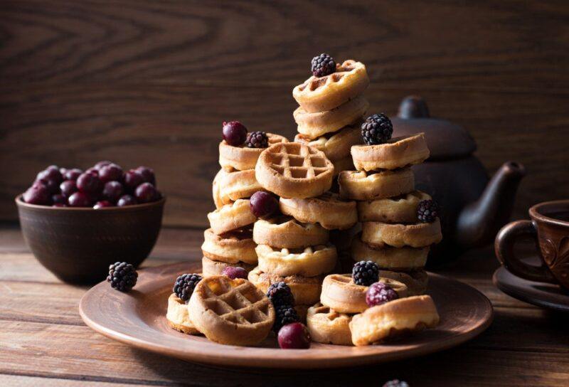 A stack of mini waffles with fresh fruit, next to a bowl of fresh fruit