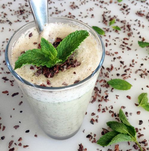 A chocolate chip smoothie in a glass with chocolate chips and mint leaves scattered around. 