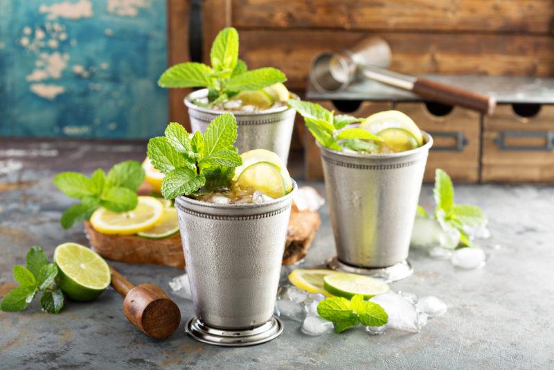 Three mint julep cocktails on a slate table with garnishes