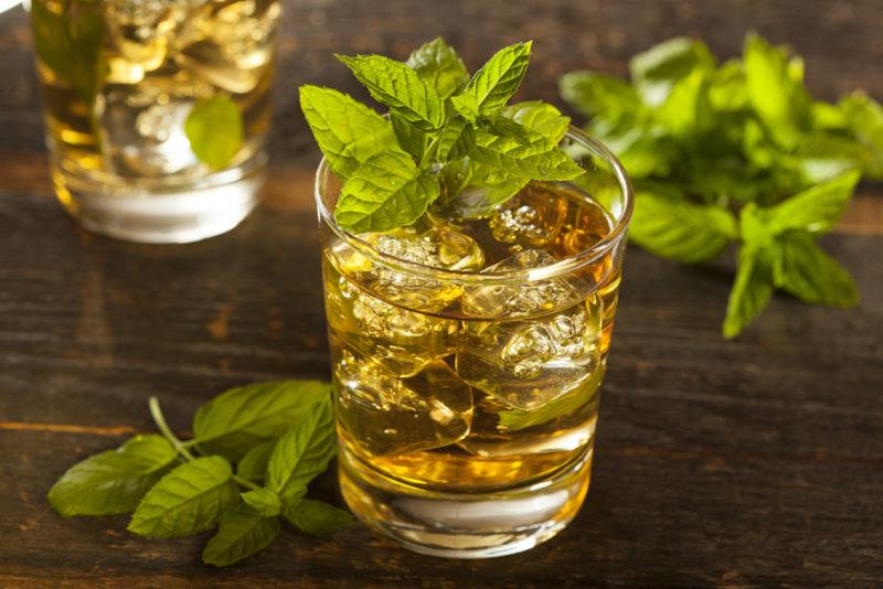 Two glasses of a mint julep cocktail with various mint leaves on the table and as a garnish