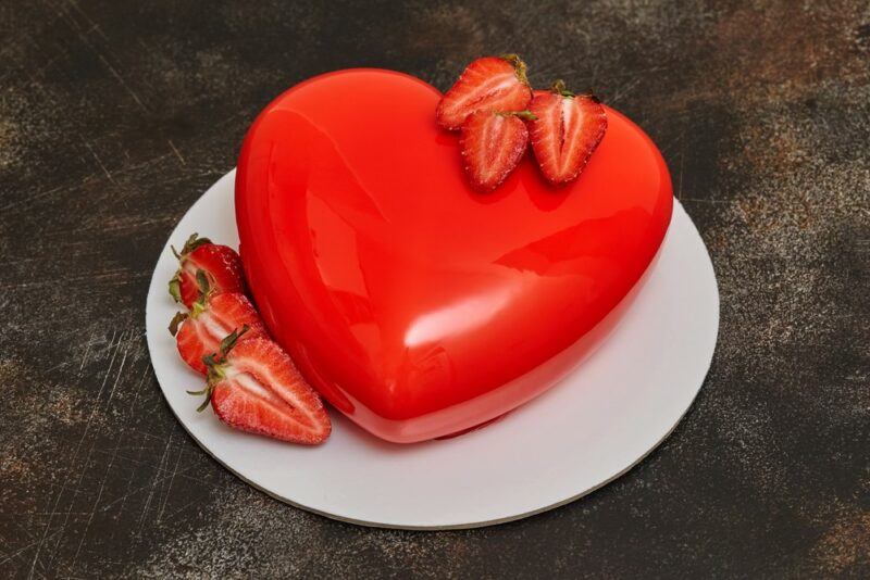 A white plate containing a love heart shaped chocolate mousse cake with a mirror finish