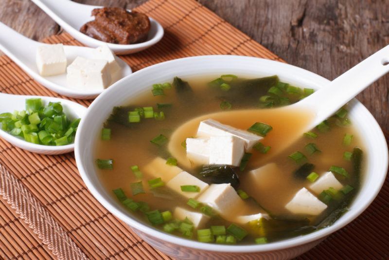 A white bowl of miso soup with tofu and a spoon