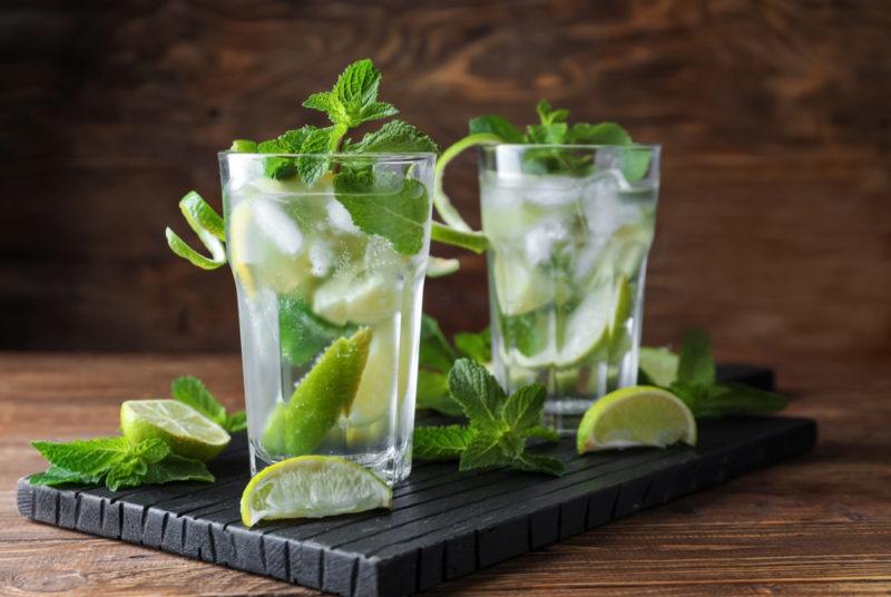 Two mojito cocktails on a board with various garnishes and other ingredients