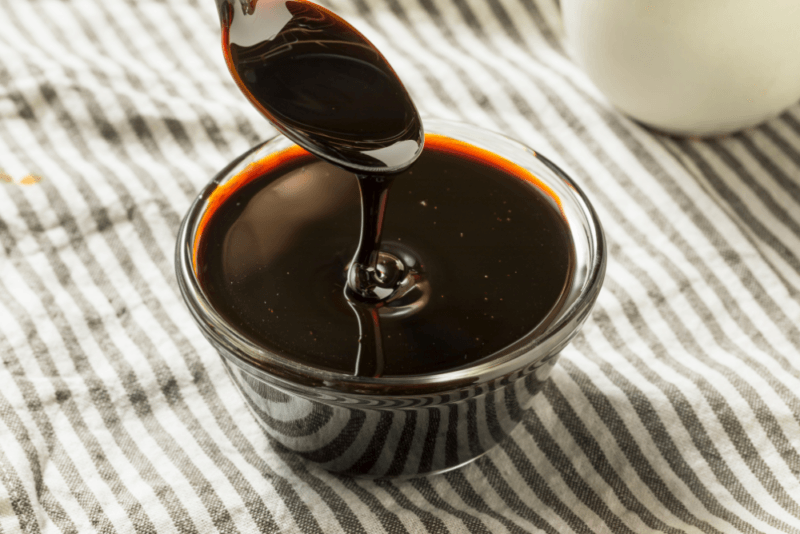 A cloth with gray and white stripes, plus a glass bowl of molasses with a spoon