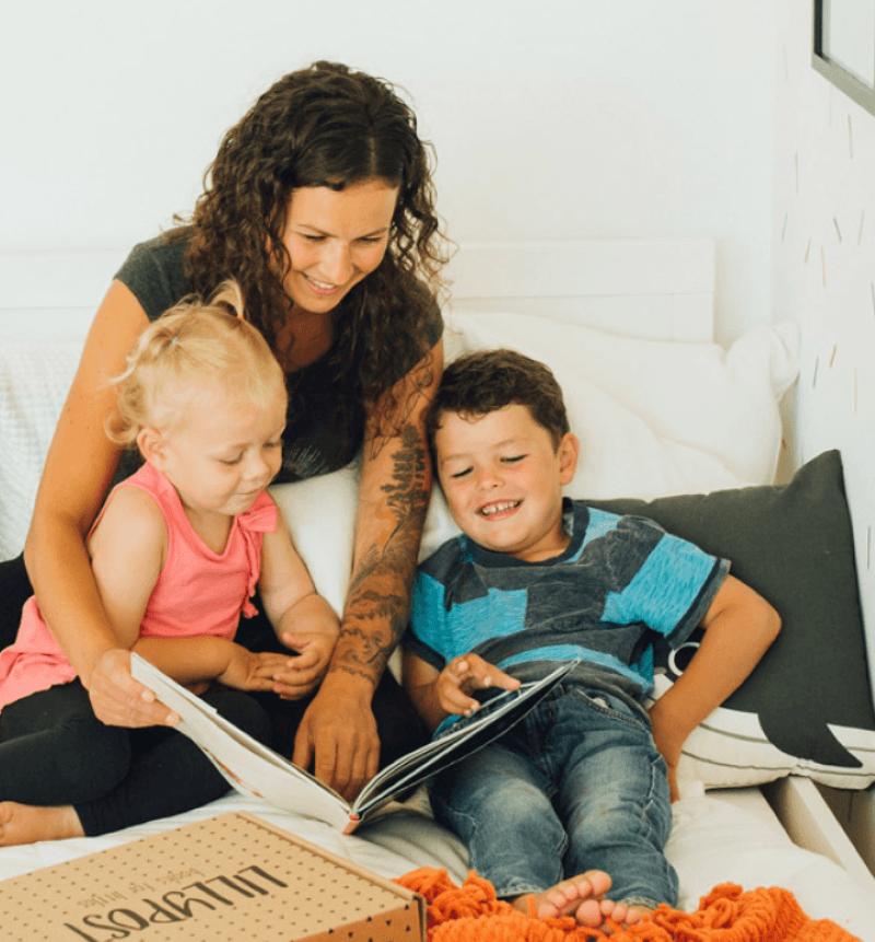 Mother with her two kids on a bed reading a book together