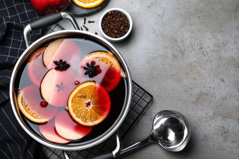 A stainless steel pot of mulled wine with oranges, next to a ladle and some spices