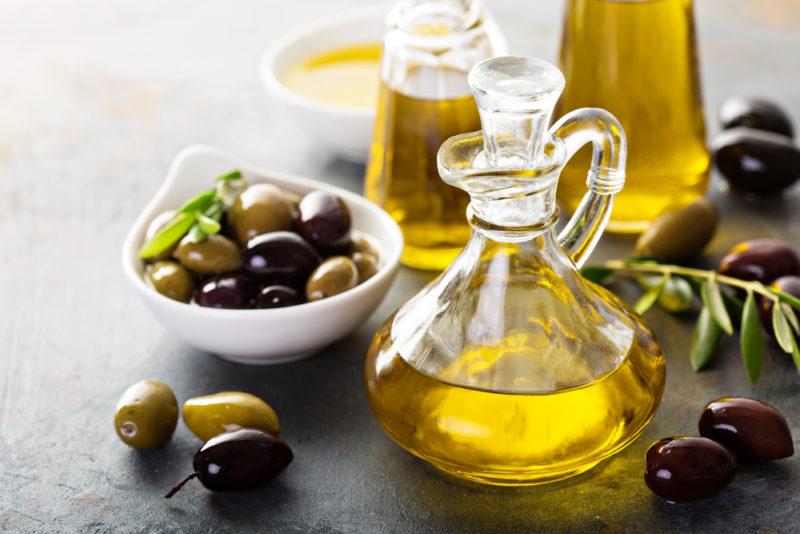 Three differently sized bottles of olive oil, with an olive brance, a dish of olive oil, and a dish of olives