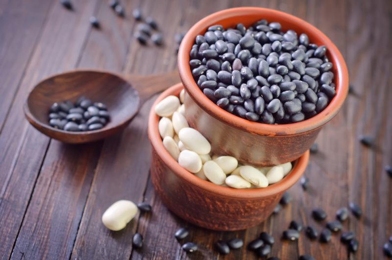 A bowl of white beans, with a bowl of black beans on top and a smaller bowl of beans on a table