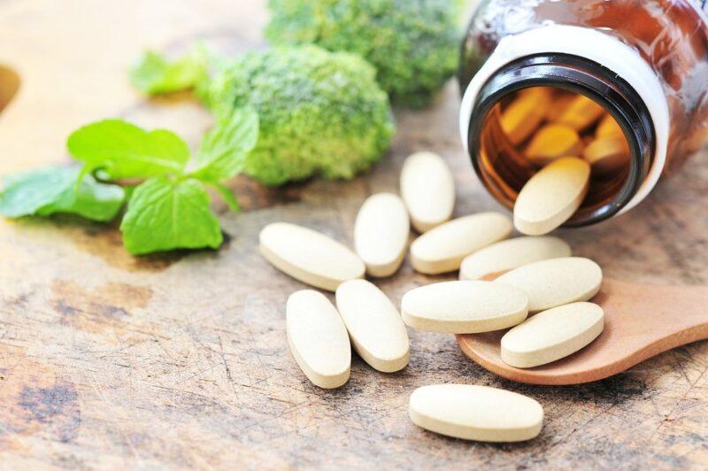 Multivitamins being poured out of a bottle next to broccoli | Food For Net A bottle of multivitamins spilling onto the table, next to some broccoli