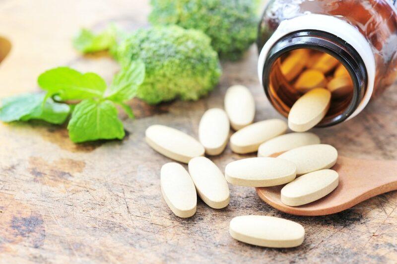 A bottle of multivitamins spilling onto the table, next to some broccoli